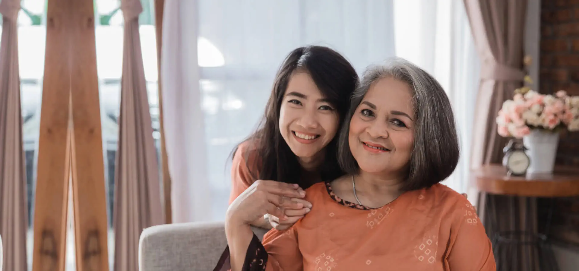 Adult daughter hugging her smiling older mother at home